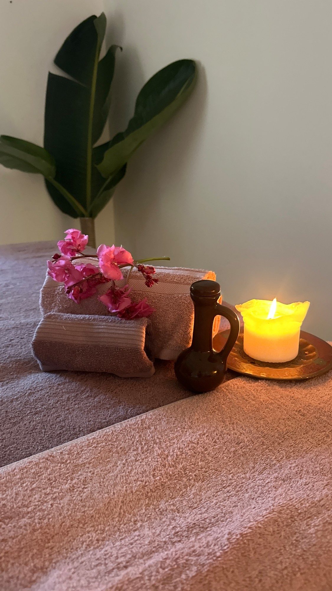Folded towels with bougainvillea, an oil jug and a lit candle on the massage table
