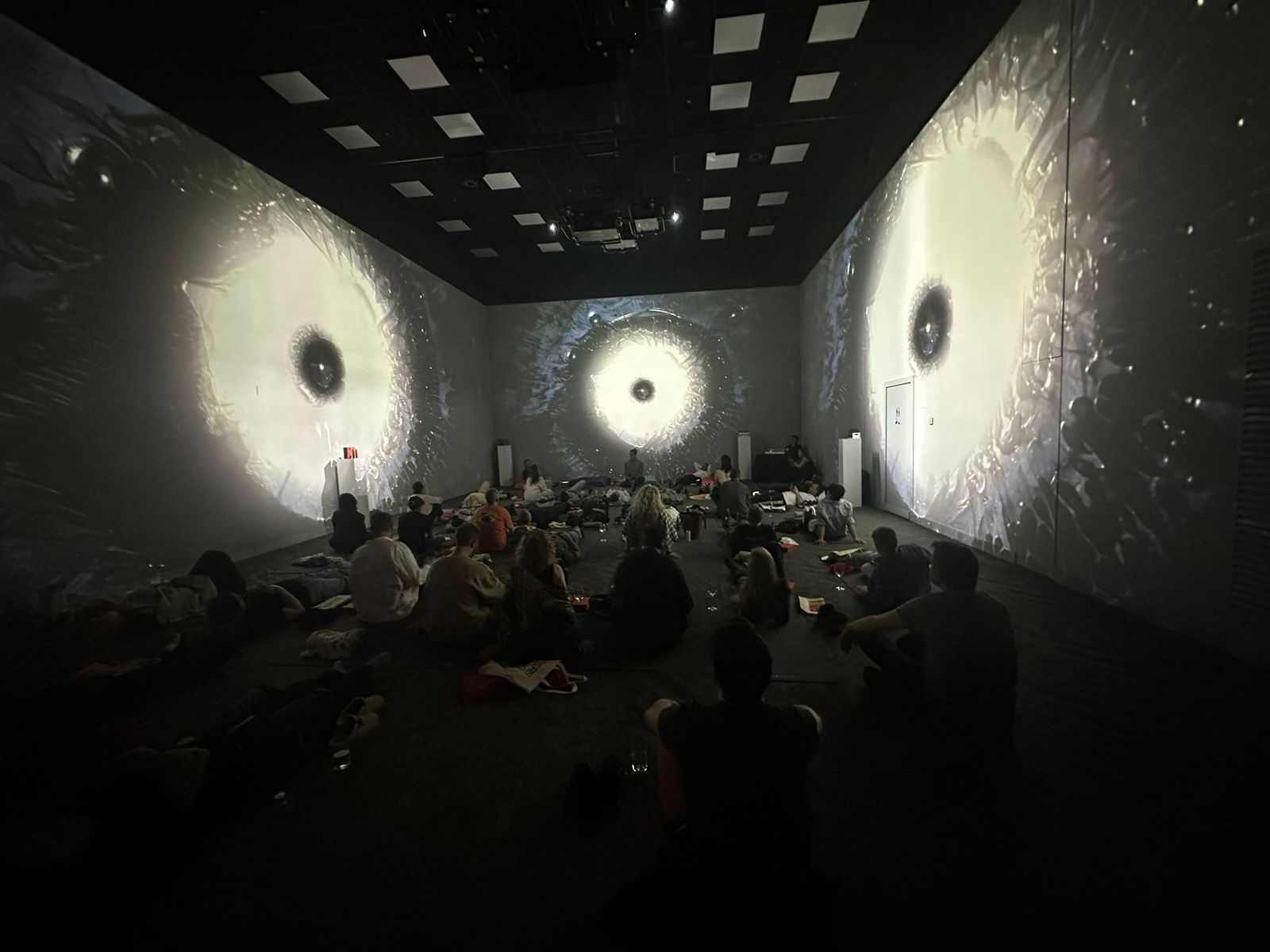 A group lying in an immersive room under large projected visuals during a Breath Lab session