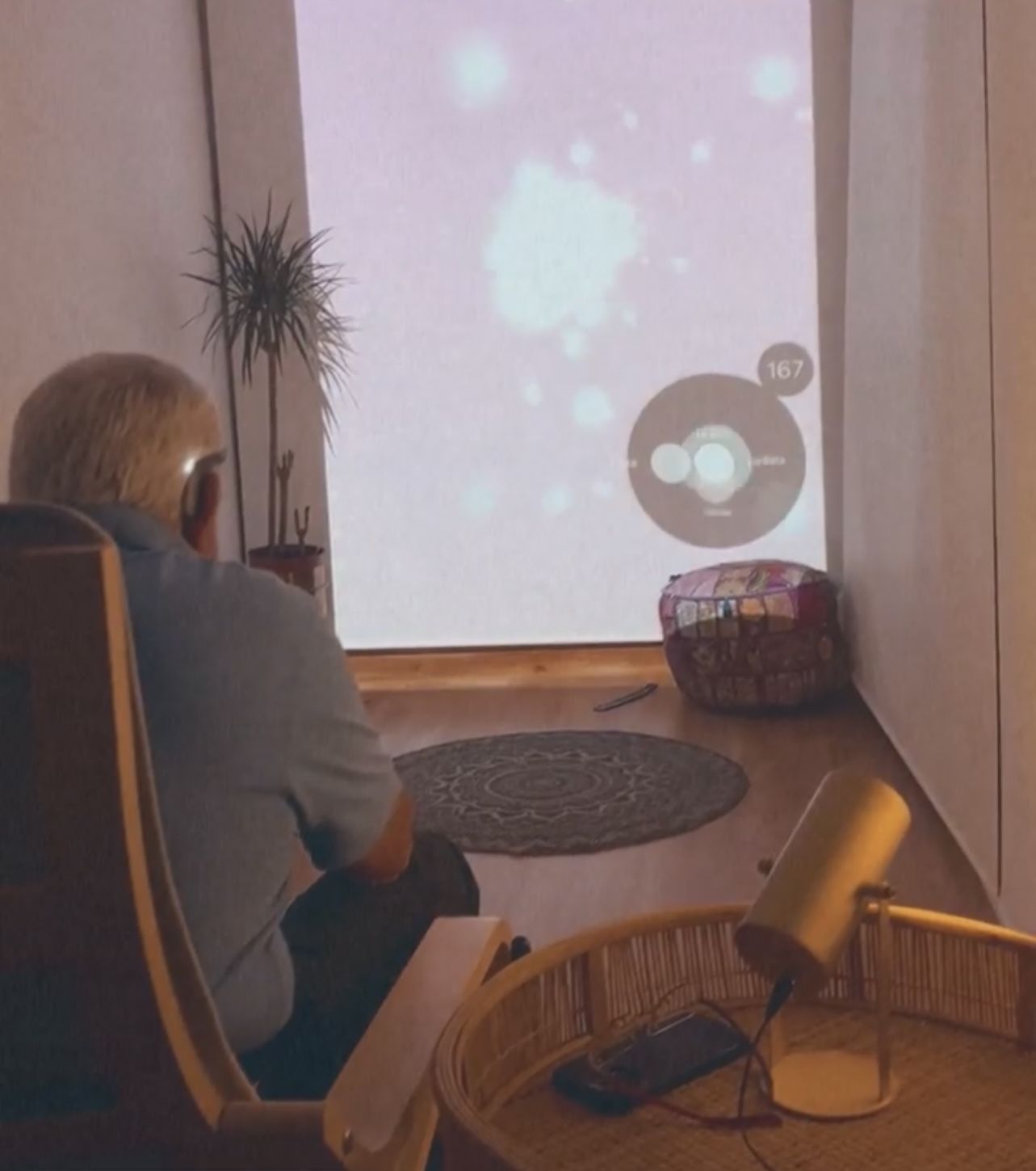 A person seated in a quiet room facing a softly lit screen during a guided practice