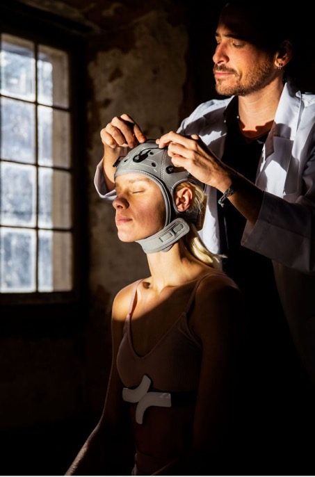 A practitioner fitting an EEG cap to a seated woman in a shaft of light