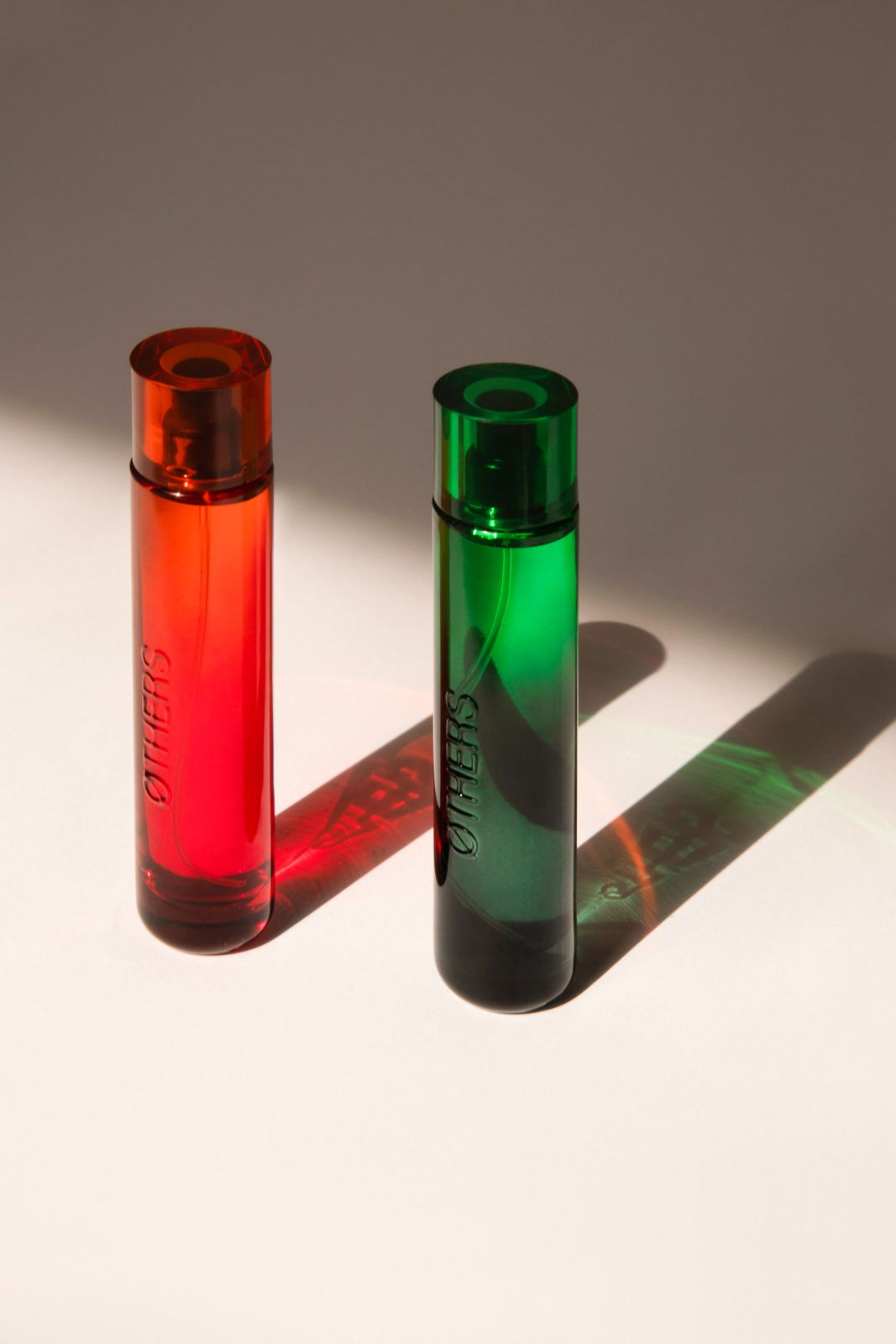 Two coloured fragrance bottles casting long shadows