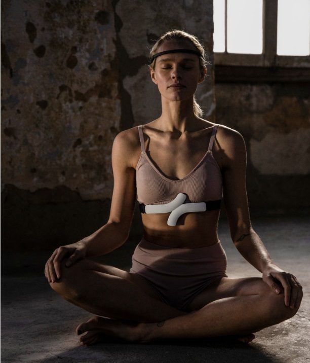 A woman meditating cross-legged with a chest heart-rate sensor, in soft window light