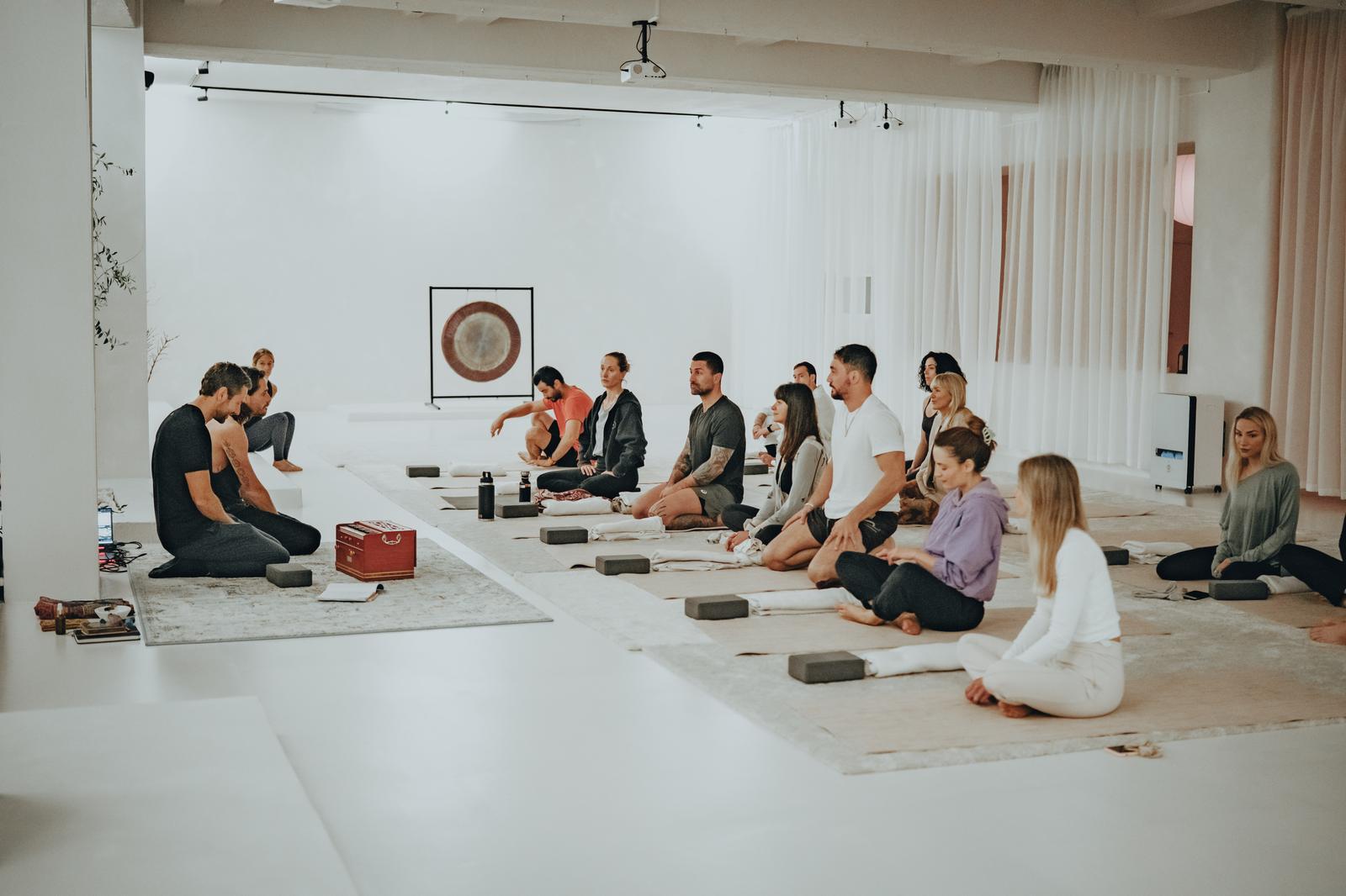 A group seated on cushions in a white studio during a guided session