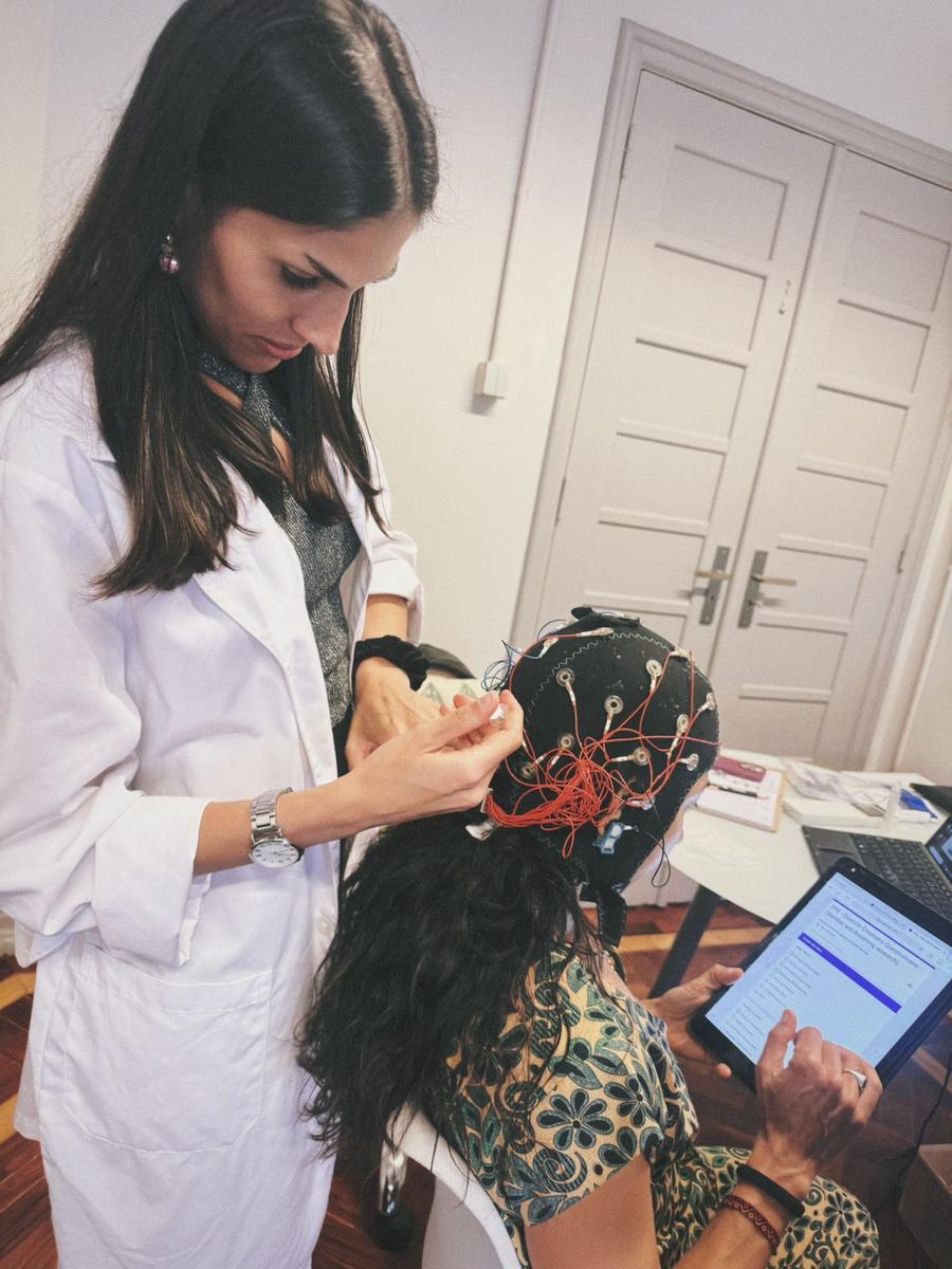 A clinician in a white coat fitting an EEG cap on a seated client