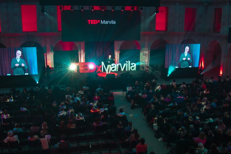 An audience in a dark hall facing a stage with red TEDx letters