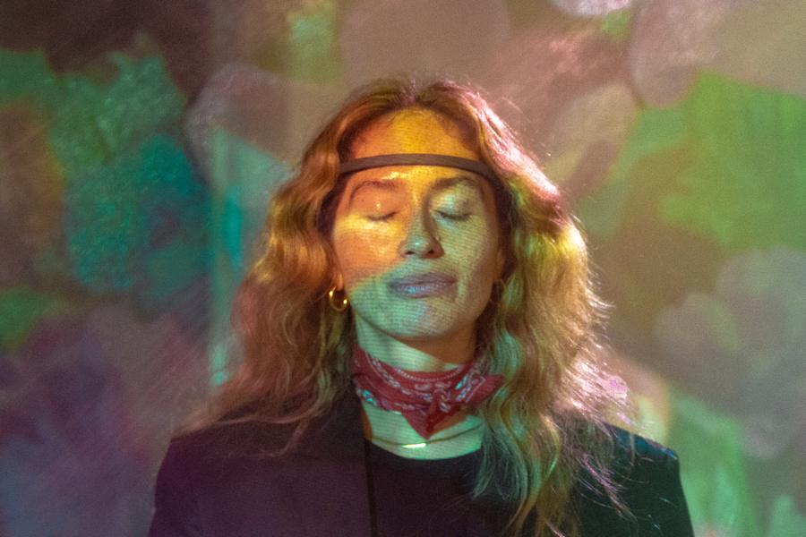 A guest wearing an EEG headband, eyes closed, under colourful projected visuals