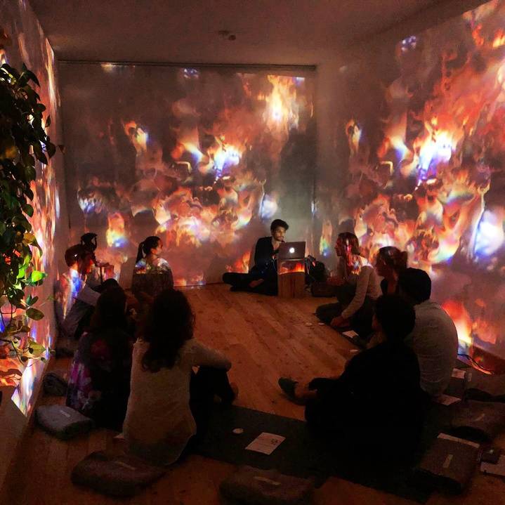 An audience seated on the floor under warm projected visuals
