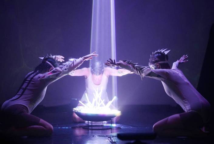 Two performers facing each other above a glowing light, hands raised