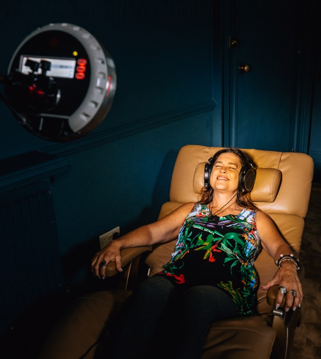 A woman reclined in a chair with headphones under a roXiva light machine