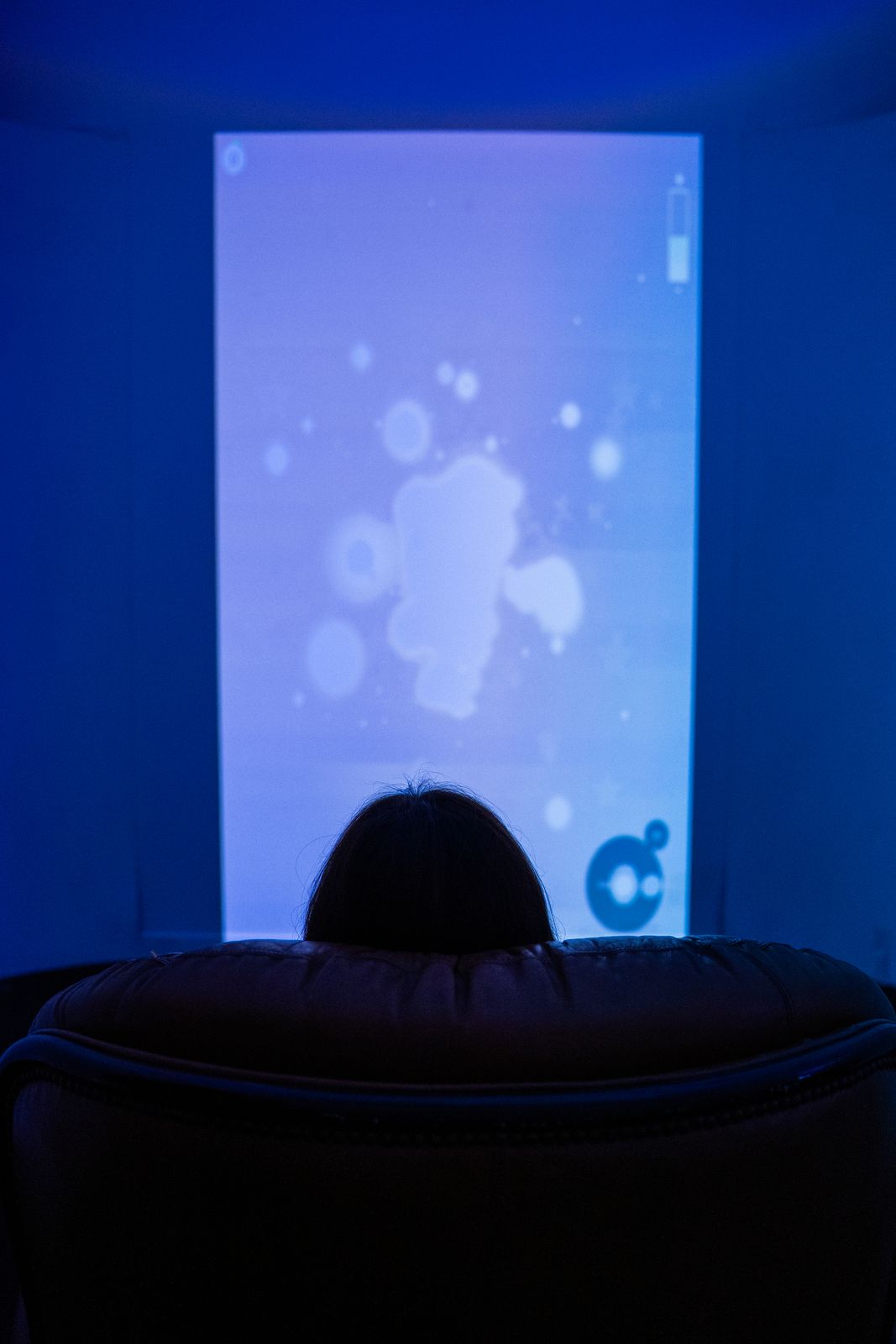 A person seated before a tall glowing blue screen in an immersive room